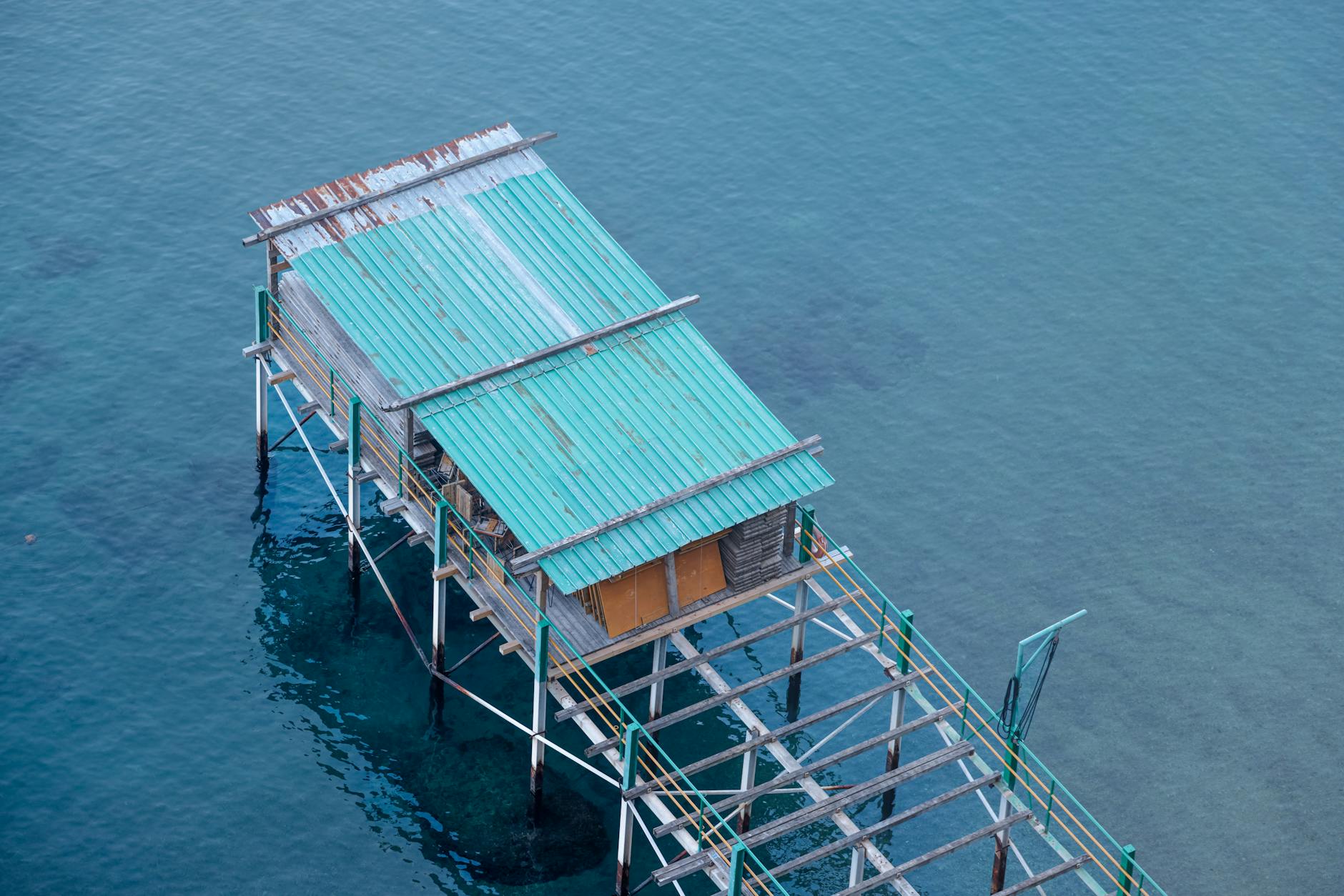 Elevated shot of a rustic stilt house over clear blue water, showcasing serene coastal architecture.