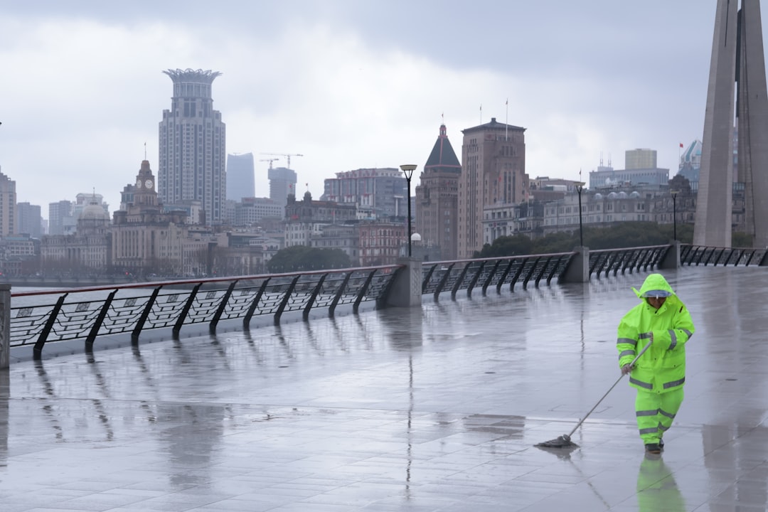 Worker in bright yellow suit sweeps wet pavement outdoors.