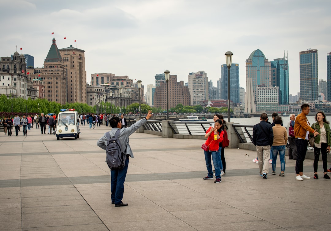 People taking photos along a waterfront with city skyline.