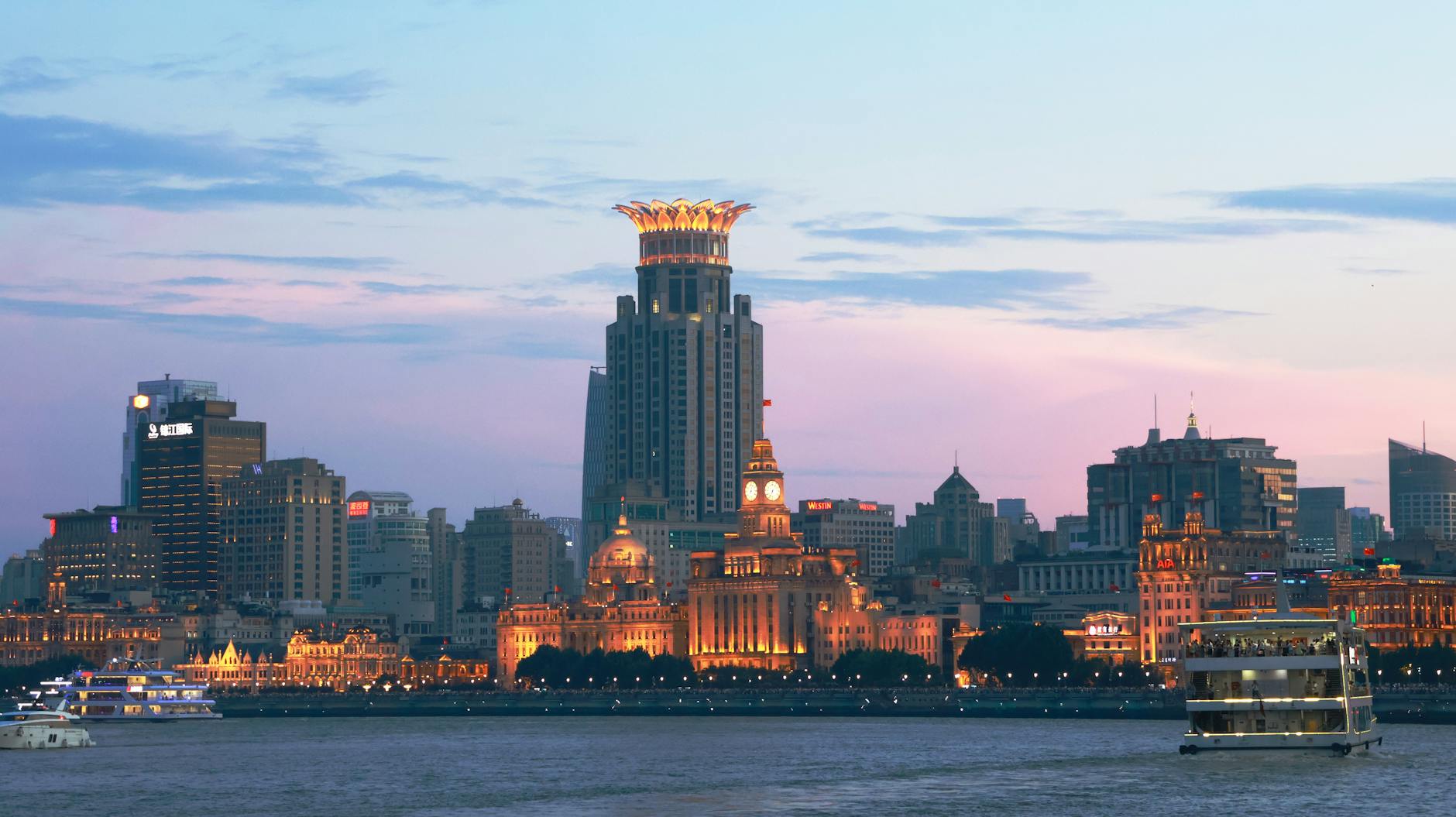 Panoramic view of the illuminated Shanghai skyline and Huangpu River during twilight with iconic landmarks.