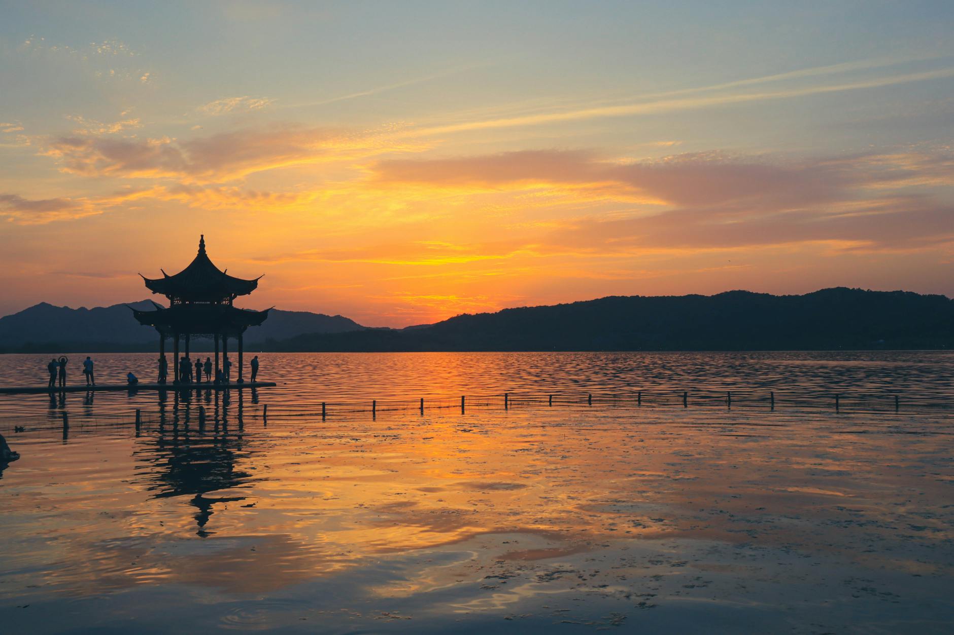 Silhouettes at West Lake in Hangzhou during a serene sunset with a traditional pagoda view.