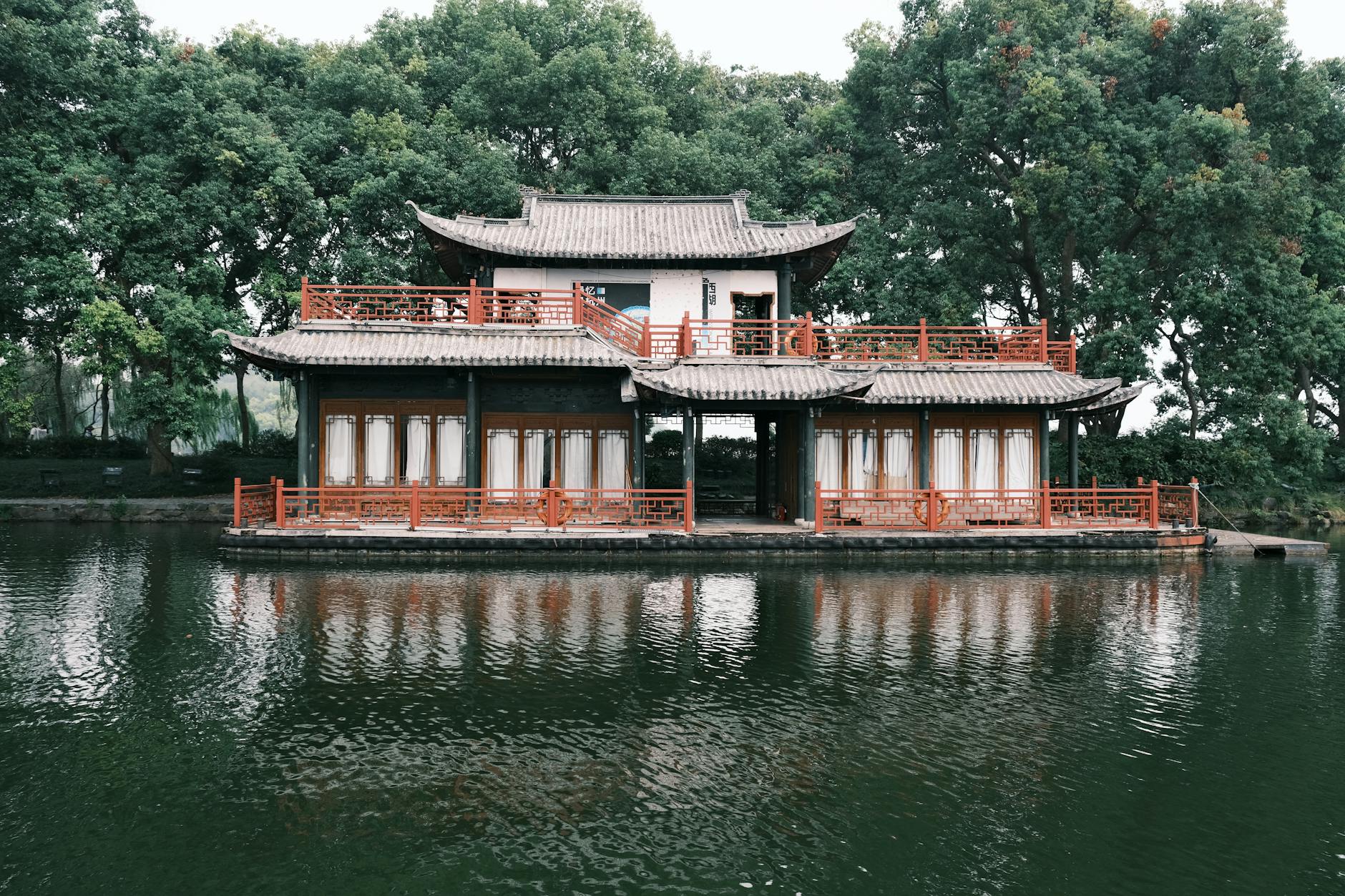 Serene view of traditional Chinese pavilion on reflecting water, surrounded by lush greenery.