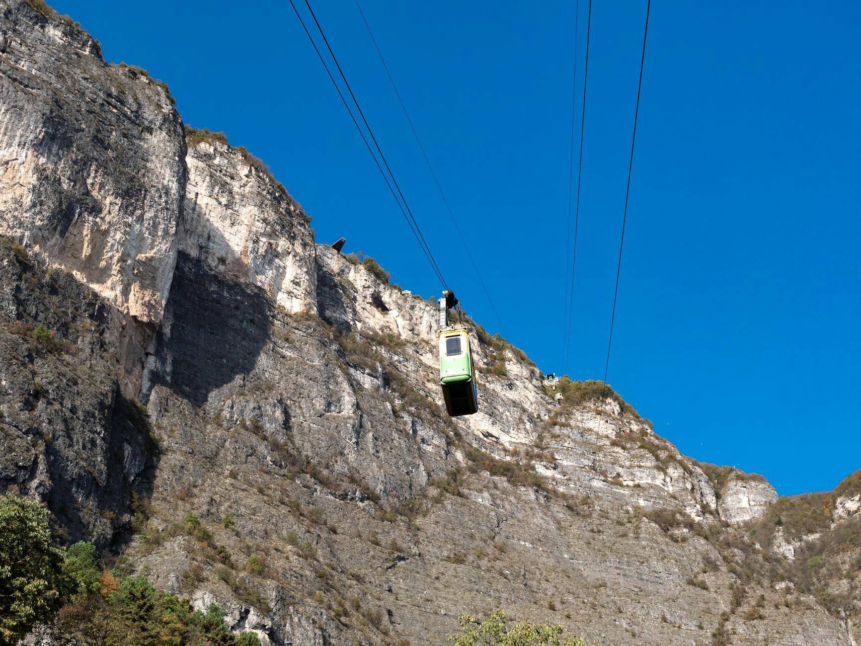 Cable car traversing rugged cliffs against a dazzling blue sky.