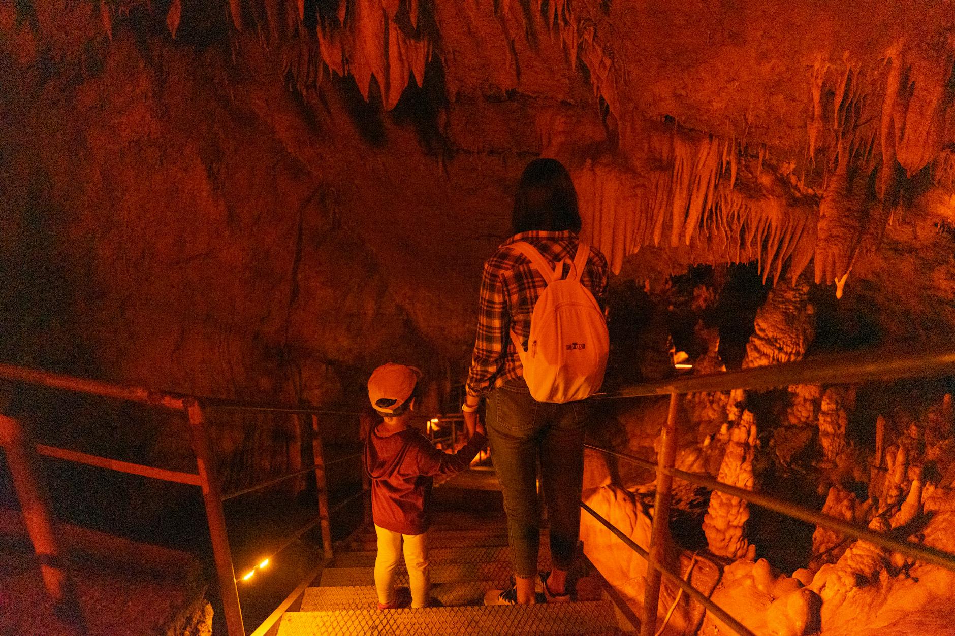 A mother and child descending stairs in a dimly lit cave, surrounded by stalactites.