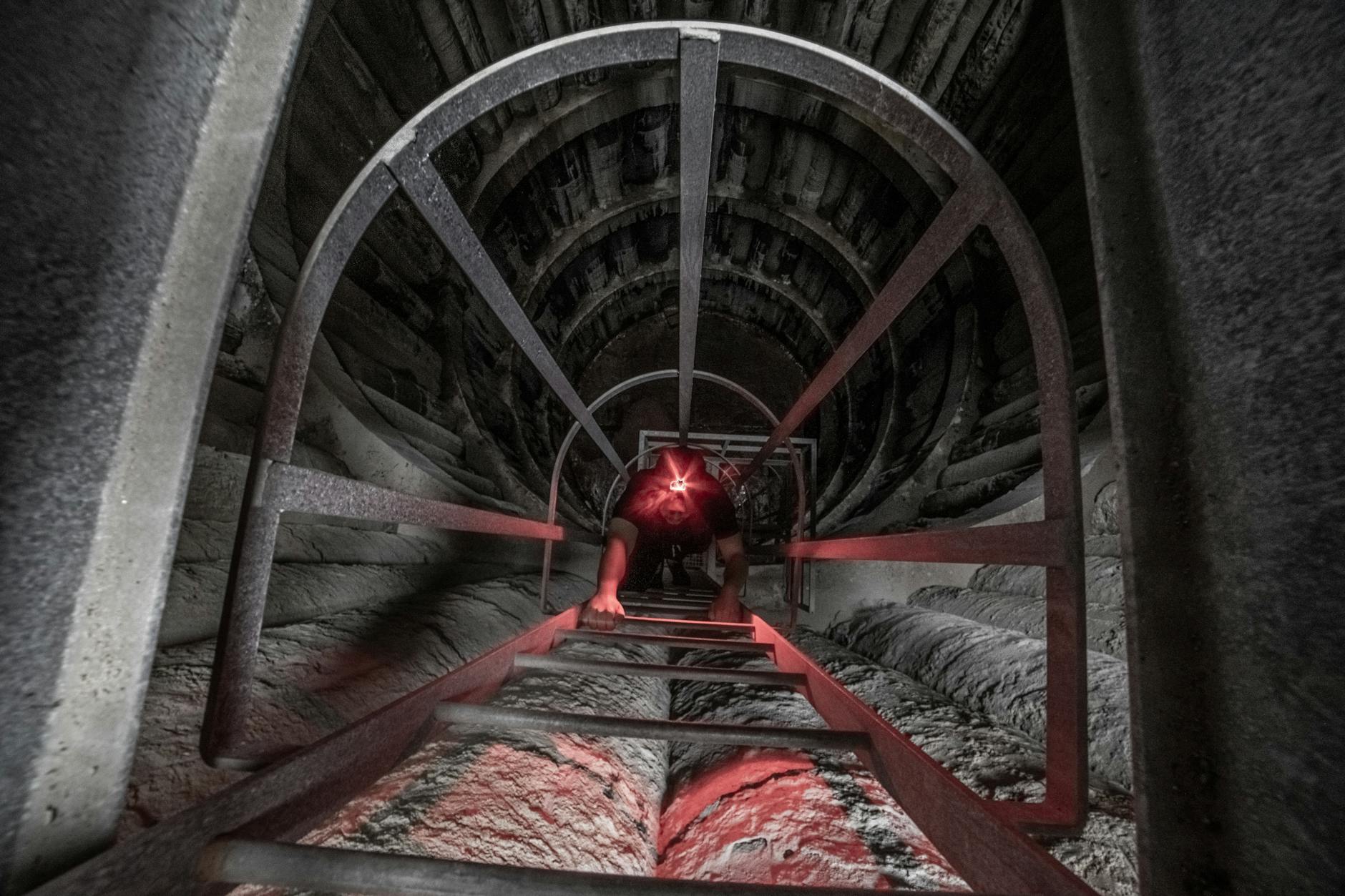 Brave adventurer climbs an industrial ladder in a dark, mysterious tunnel with a headlamp.
