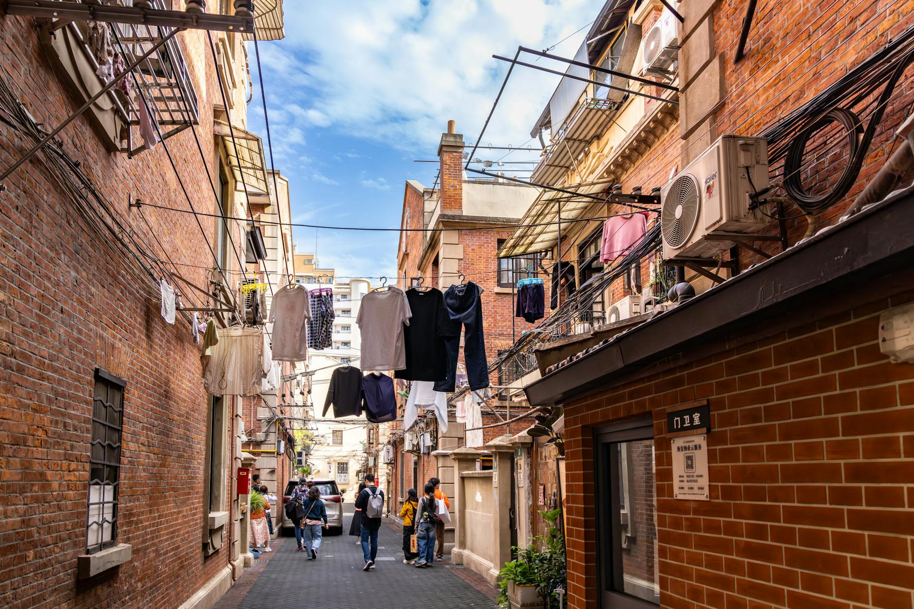 Bustling Shanghai alleyway with laundry, brick buildings, and pedestrians.