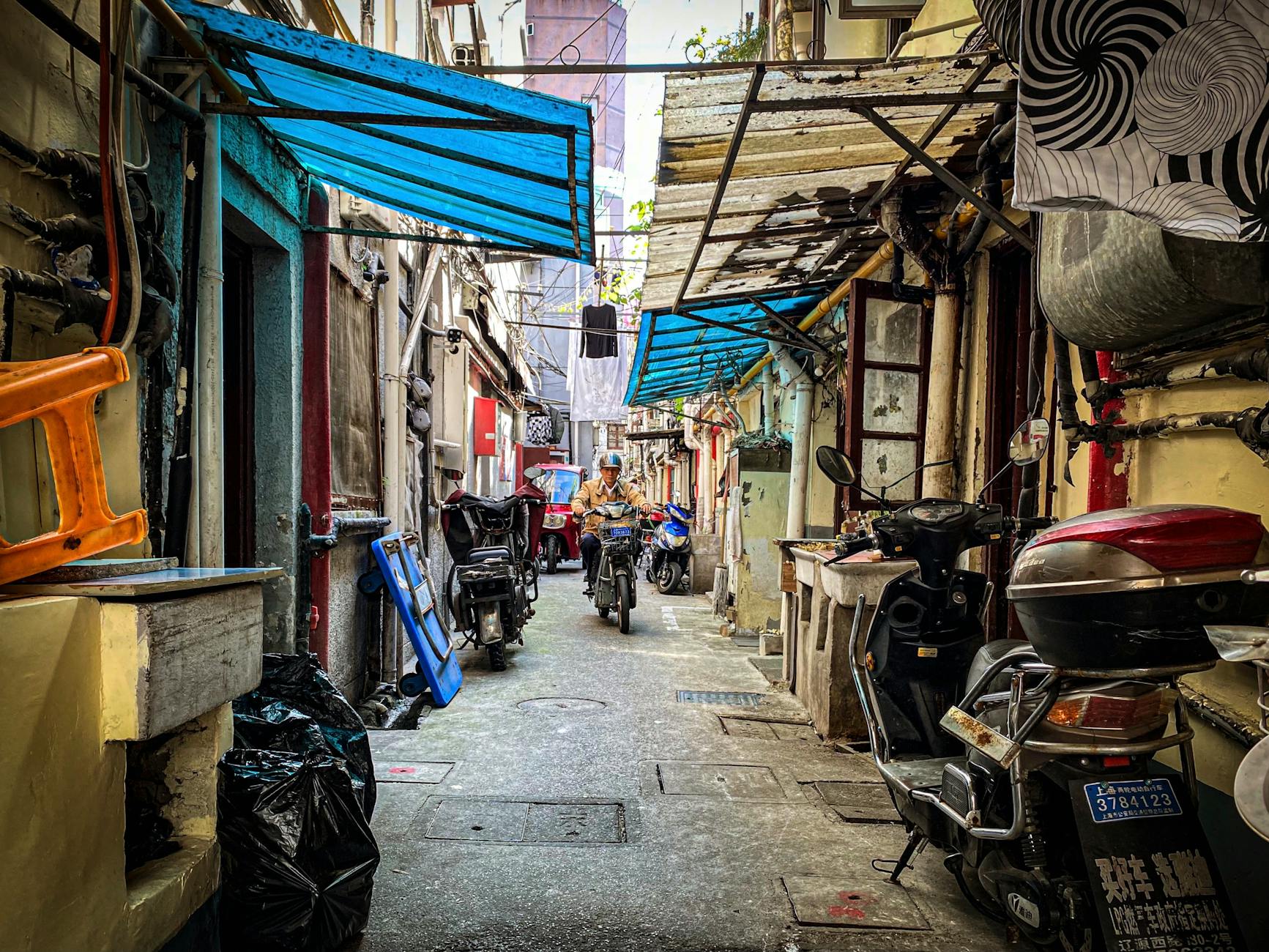 A bustling narrow alley with motorcycles, vibrant canopies, and a rider.
