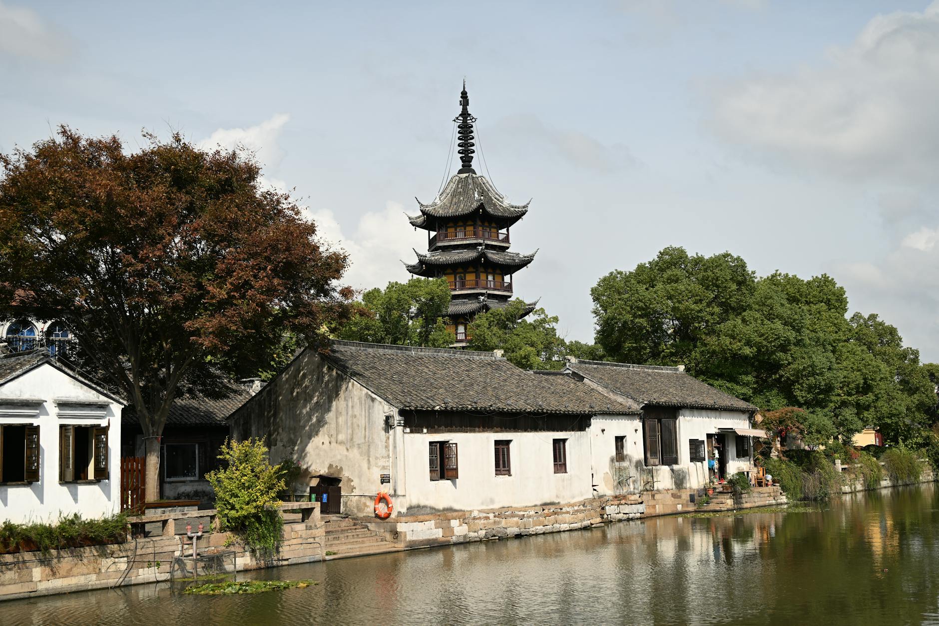 Scenic view of a traditional Chinese pagoda by the water with lush greenery and blue sky.