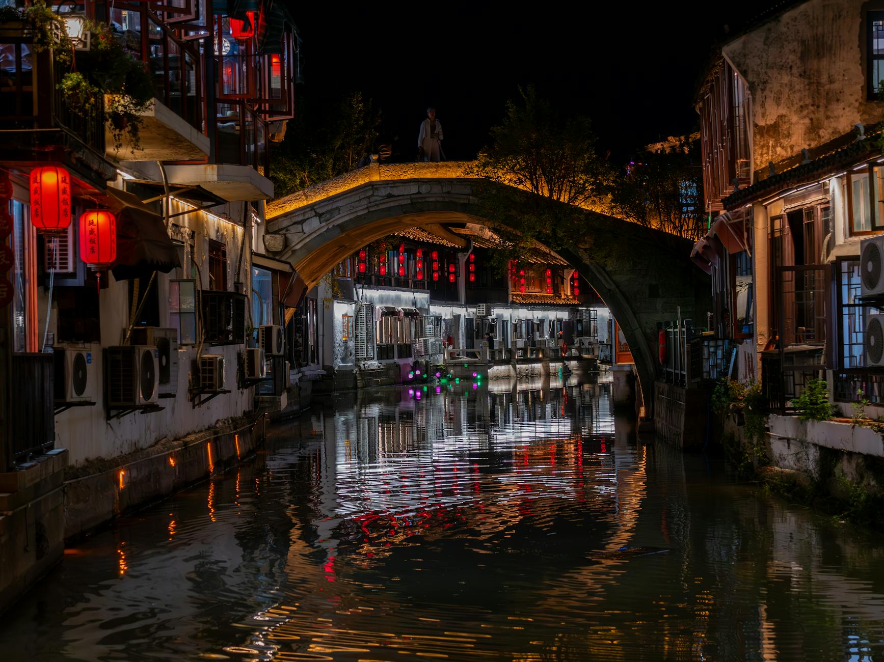 Scenic night view of illuminated canal and bridge in Suzhou, China, reflecting vibrant lights.