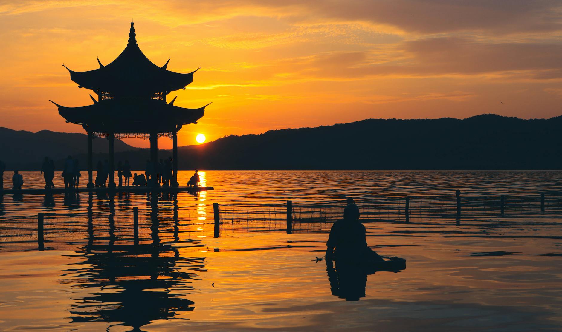 Tranquil evening scene of West Lake, Hangzhou, with a silhouette of a pavilion against a stunning sunset.