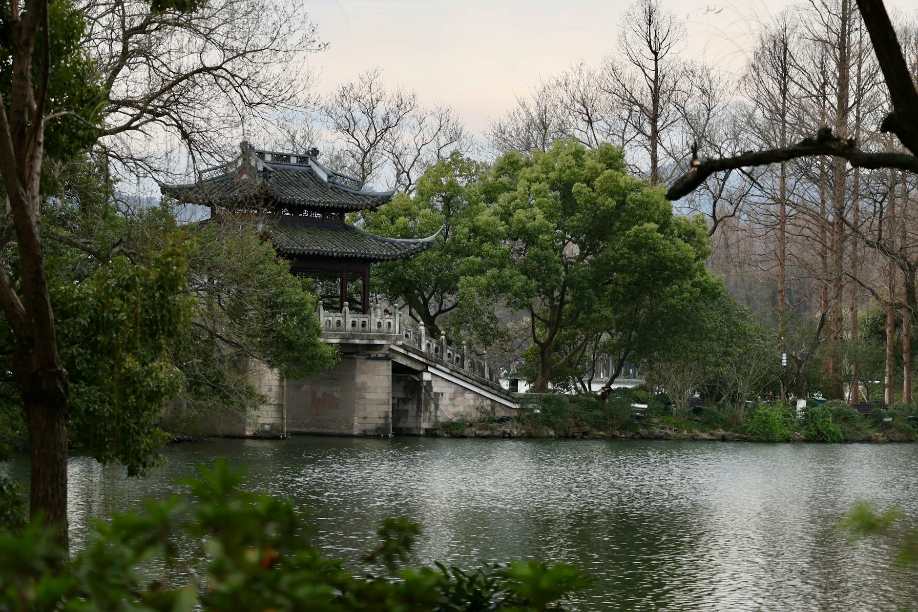 A peaceful traditional Chinese pavilion nestled by a tranquil lake amid lush trees in Hangzhou, China.