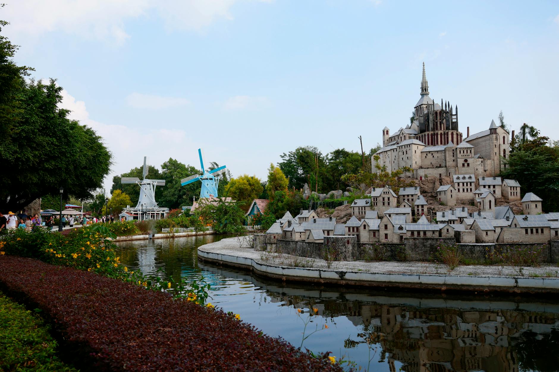 Explore a scenic park featuring a miniature European village and windmills beside a serene pond.