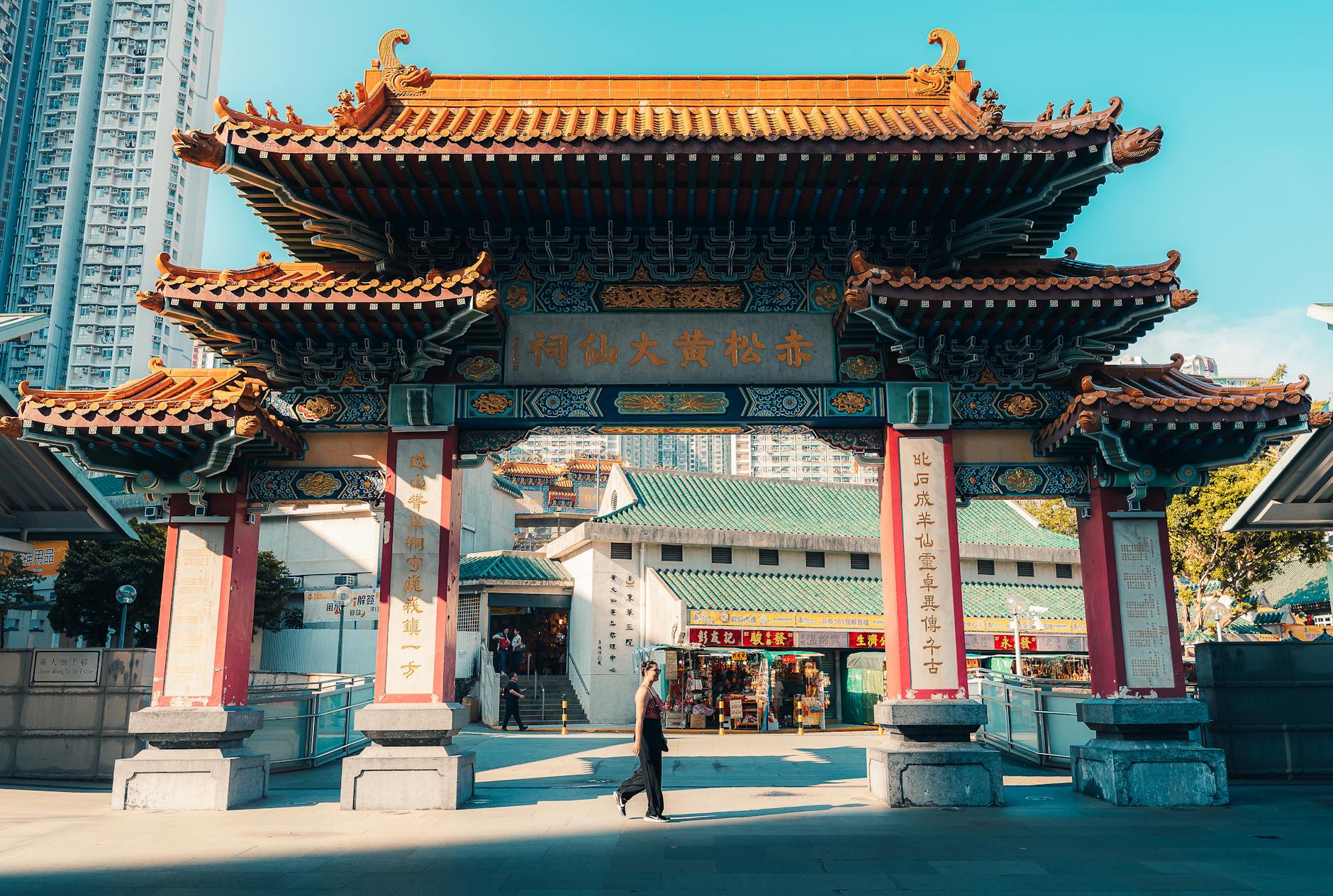 A vibrant view of Wong Tai Sin Temple in Hong Kong with clear blue skies and people walking by.