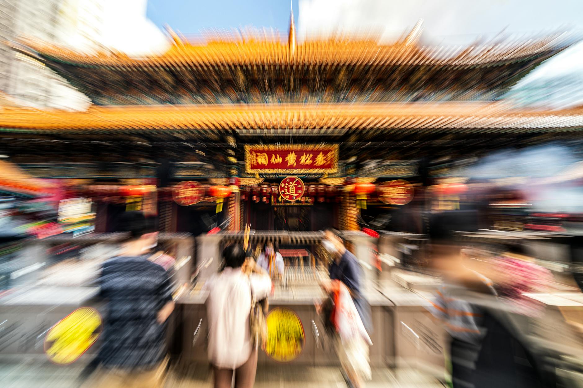 Dynamic, blurred scene at Wong Tai Sin Temple entrance, capturing vibrant traditional architecture.