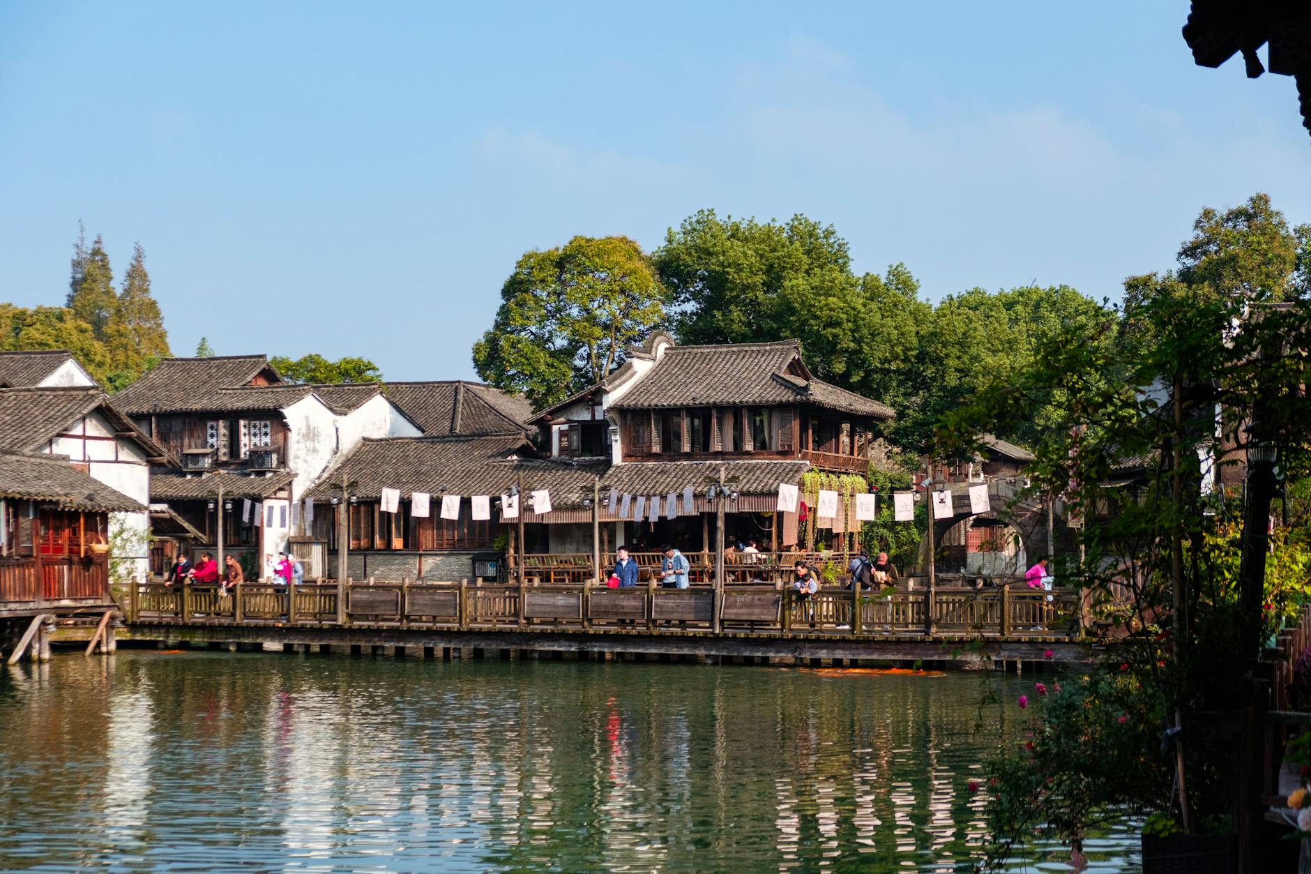 Charming view of a traditional Chinese water town with wooden houses, walking bridge, and lush greenery.