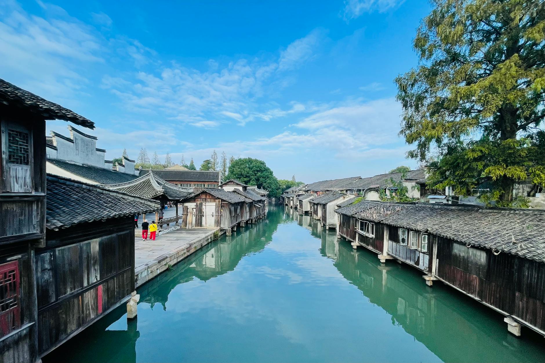 Explore the tranquil beauty of a traditional Chinese water town with ancient architecture by a calm river.
