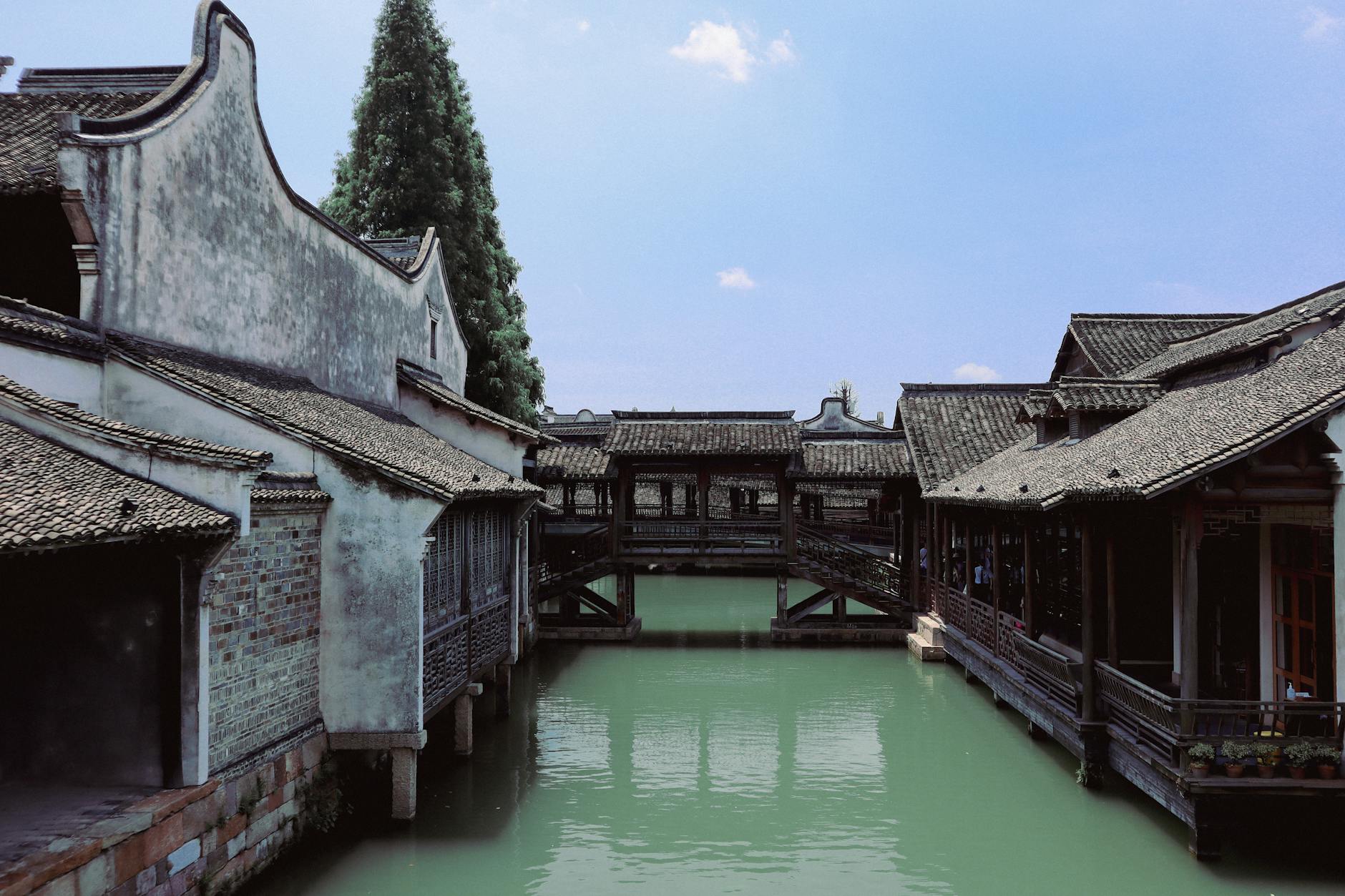 Charming Chinese water town scene with traditional architecture over a tranquil canal, clear sky.