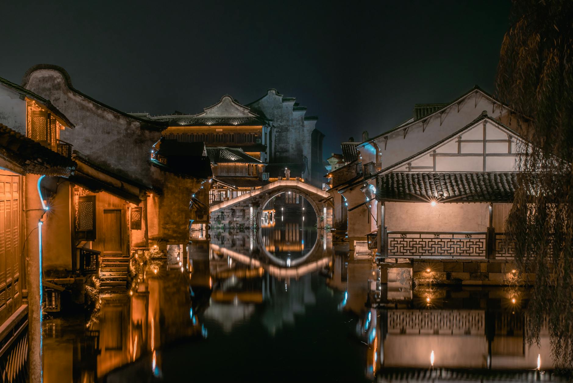 Aged house exteriors with ornamental walls reflecting in pond with pure water under dark sky at dusk