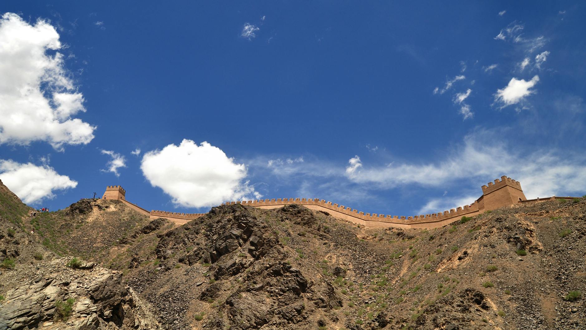 A scenic view of an ancient wall on a rocky hill under a vibrant blue sky with clouds.