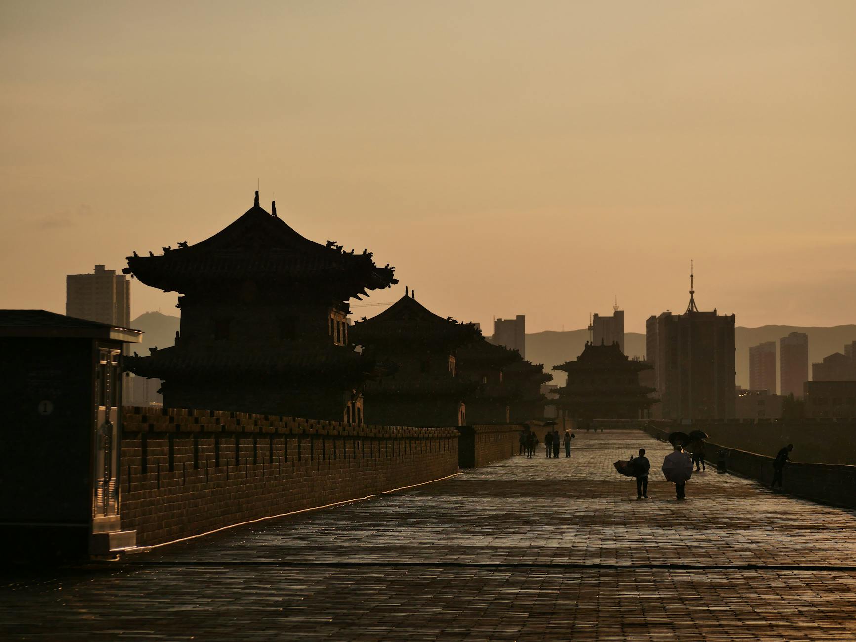 Silhouetted skyline of traditional and modern architecture at sunset along historical city wall.