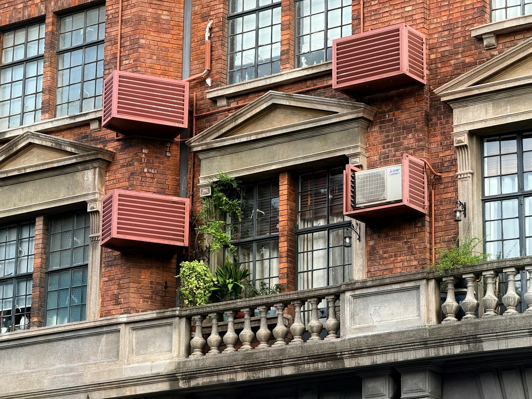 Close-up view of a red brick building with air conditioners and greenery on a balcony in Shanghai.