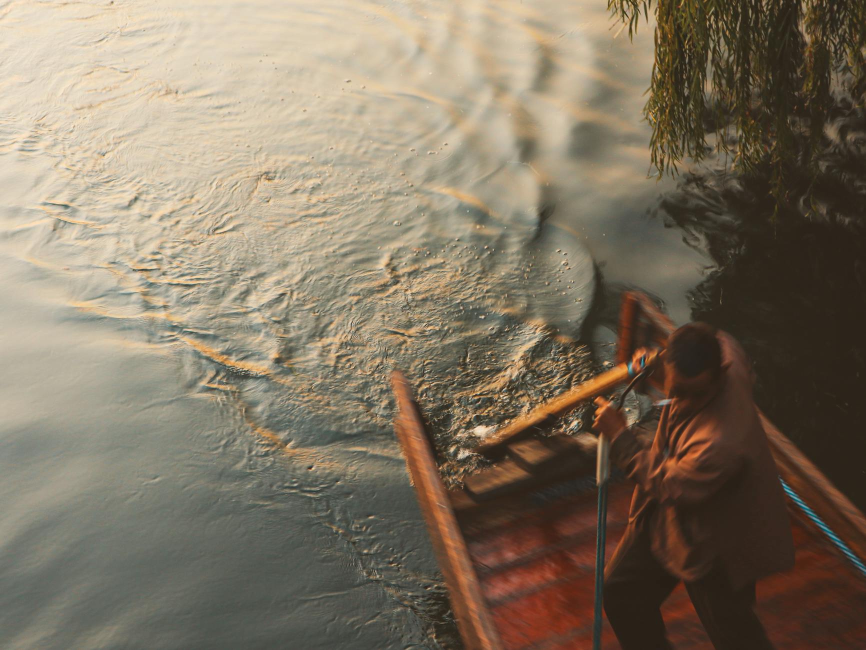 Man standing and rowing a traditional boat on West Lake, Hangzhou, during sunset.