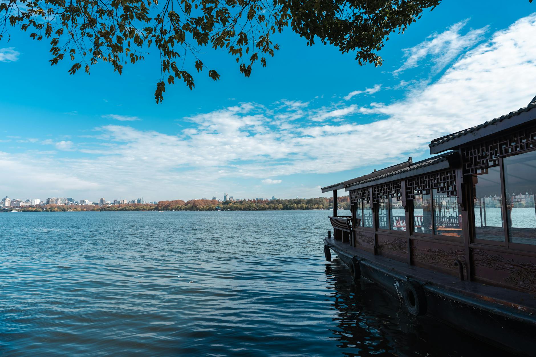 Serene view of a traditional boat on West Lake in Hangzhou, China, under clear blue skies.