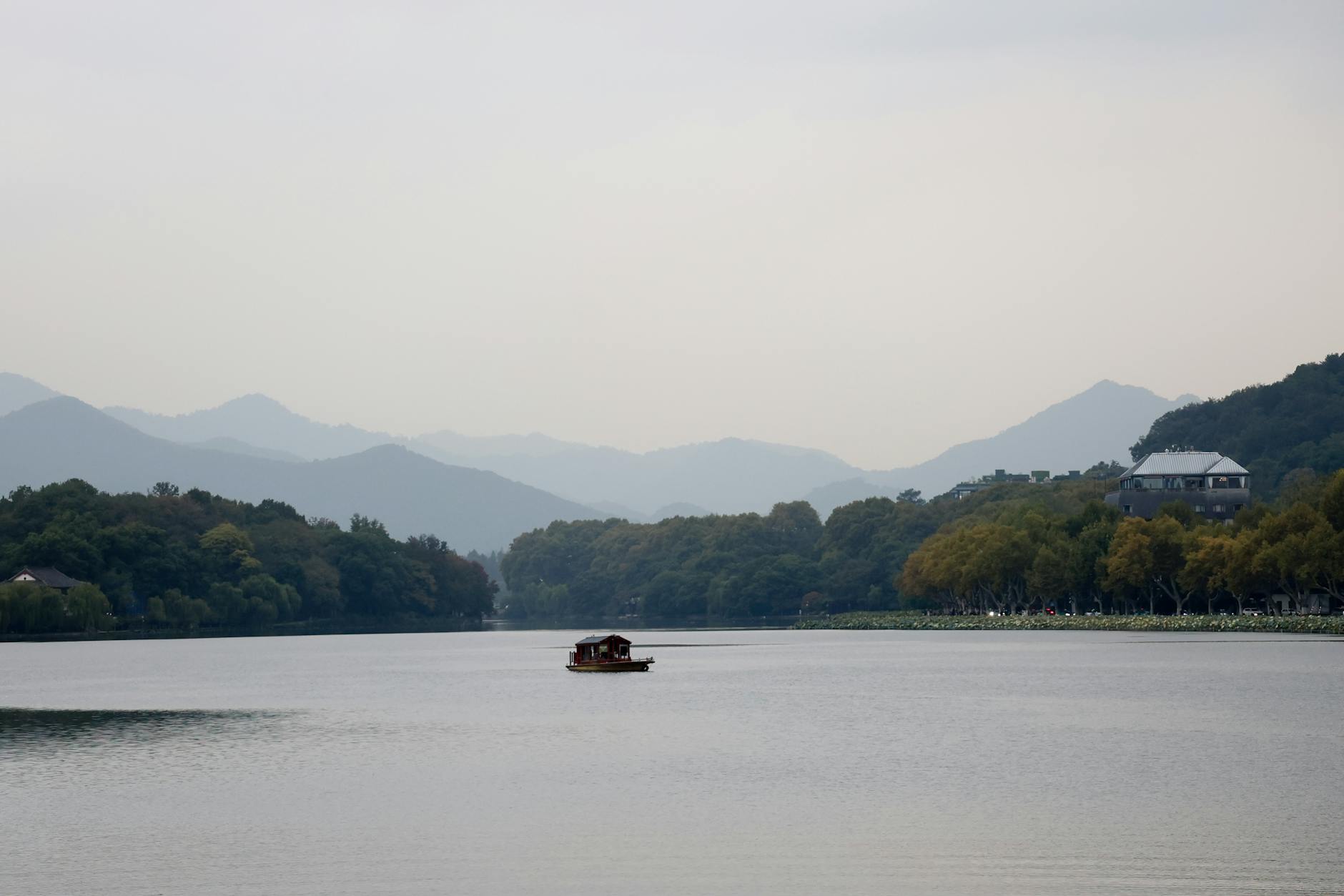 A peaceful view of West Lake with a traditional boat and mountains in Hangzhou, China.