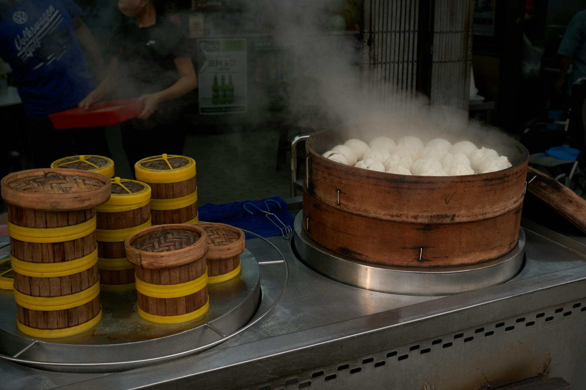 Freshly steamed Chinese bao buns in bamboo baskets at an outdoor street food stall.