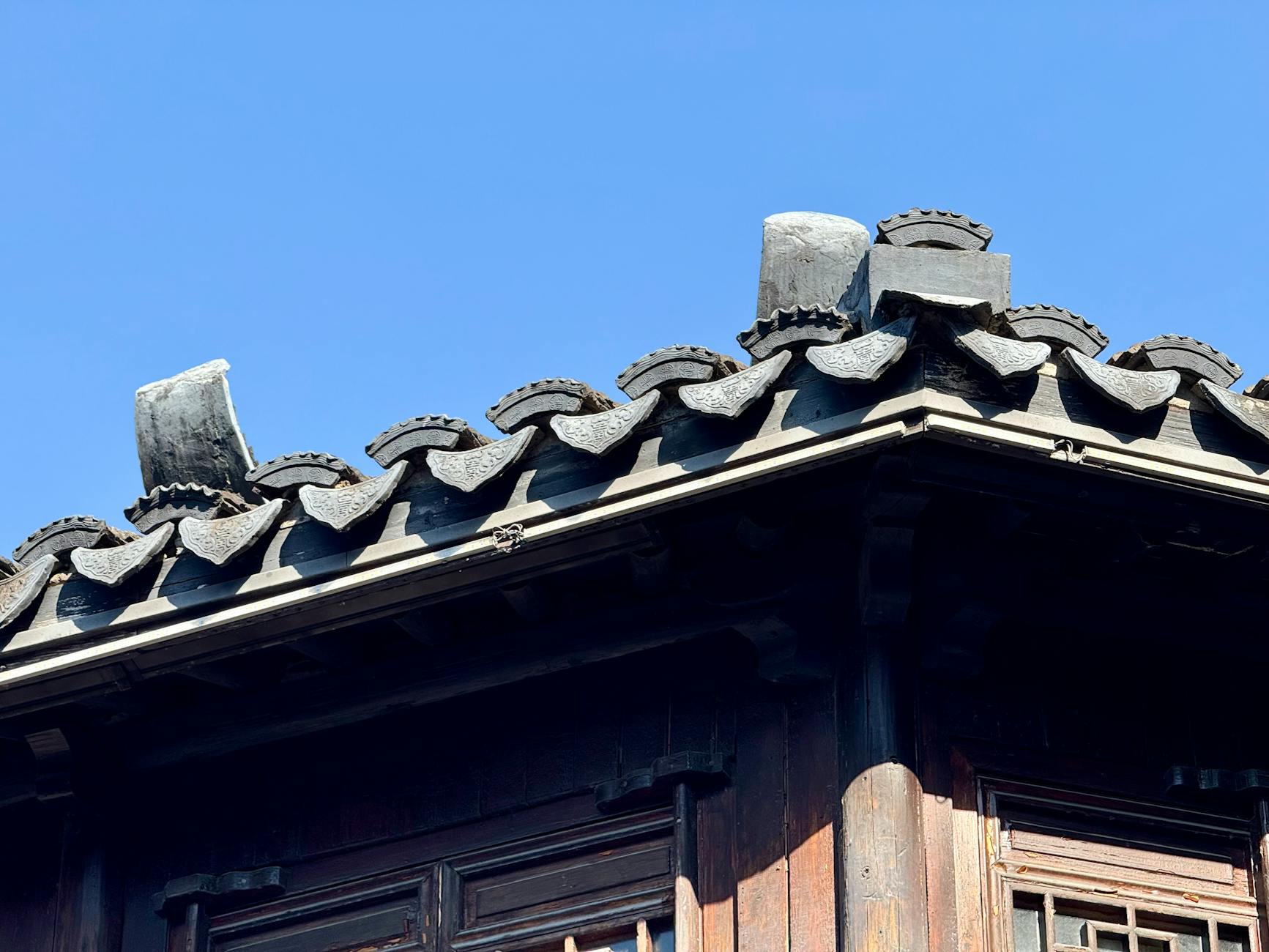 Close-up of traditional Chinese roof tiles, wooden architecture under a clear blue sky.
