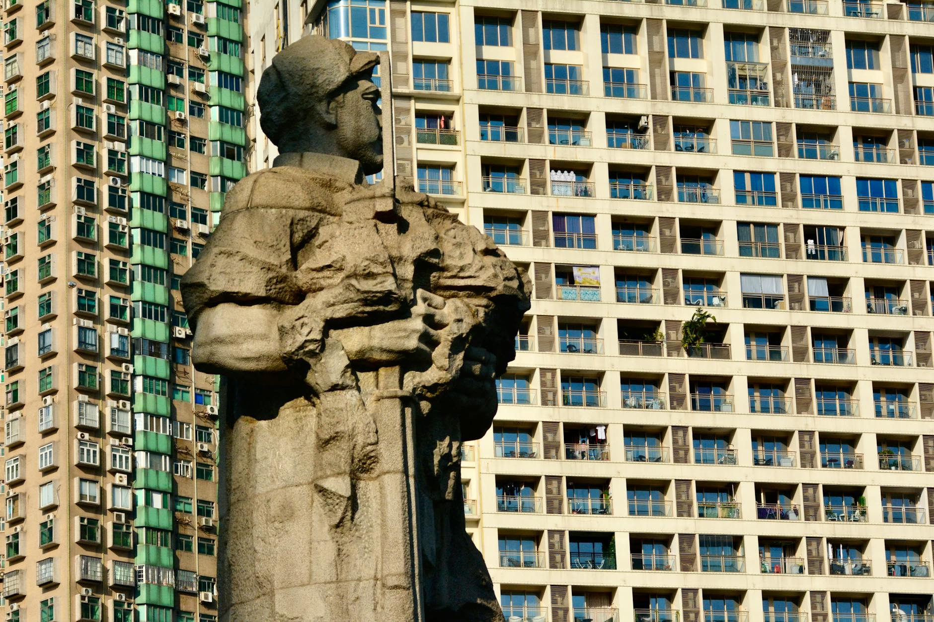 A stone statue stands against the backdrop of modern high-rise buildings in Guangzhou.