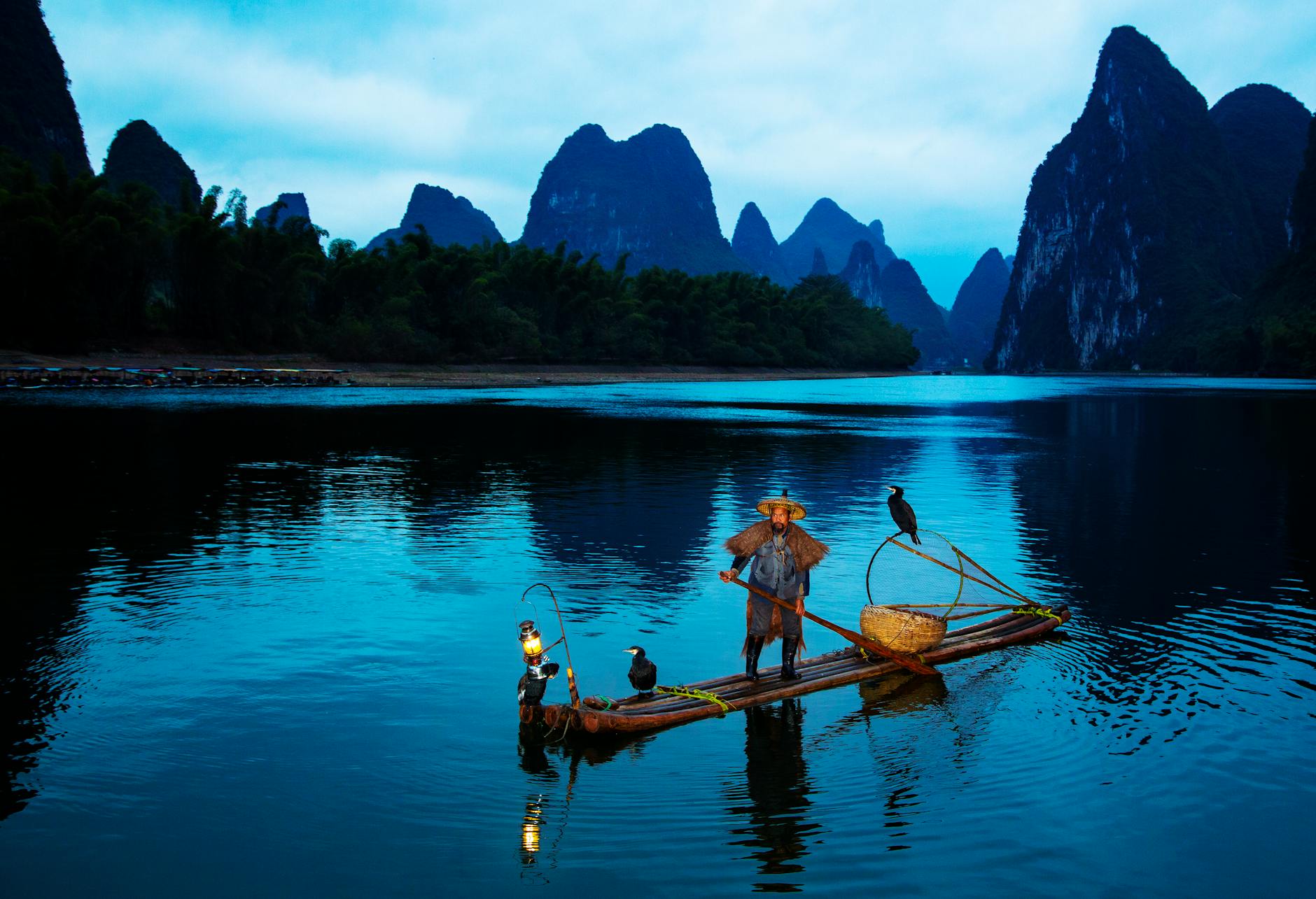 A serene scene of a cormorant fisherman at dusk on the Li River in Guangxi, China.